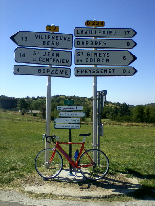 Vélo posé devant les panneaux indiquant les circuits de l'Ardéchoise : les Gorges, La Méridionale, La Chataîgne